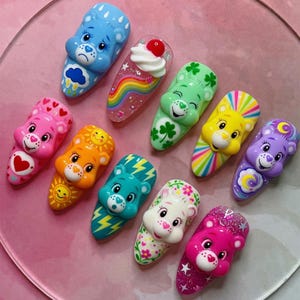 May include: A collection of ten colorful hair clips featuring 3D Care Bear character faces. Each clip displays unique designs including rainbows, hearts, clovers, suns, lightning bolts, stars, and a sundae, rendered in vibrant shades of blue, pink, orange, green, yellow, and purple.
