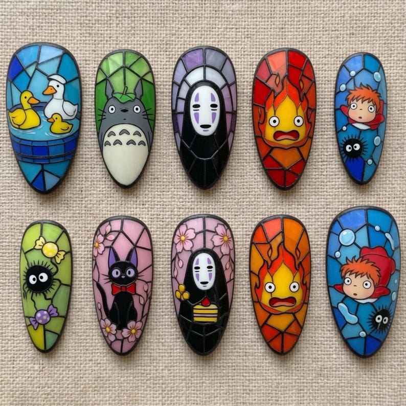 May include: Ten almond-shaped nail art tips featuring stained glass style illustrations of various animated characters, including a duck, Totoro, No-Face, Calcifer, Ponyo, a soot sprite, and a black cat, all outlined in black with vibrant colors.