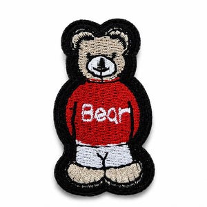 Może przedstawiać: Haftowana naszywka przedstawiająca beżowego misia z czarnym konturem. Miś ma na sobie czerwony sweter z wyszytym białymi literami napisem Bear na piersi oraz białe spodenki. Całość wzoru wykończona jest grubym, czarnym, wyszywanym obramowaniem.
