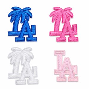 May include: Four embroidered patches featuring the letters LA in a block font. Three patches include a palm tree graphic integrated with the letters. The colors are royal blue, hot pink, white, and light pastel pink, each with a stitched border.