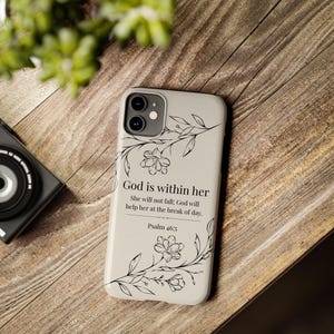 May include: A light-colored phone case with a floral design and the text "God is within her." The case also includes the text "She will not fall; God will help her at the break of day. Psalm 46:5."