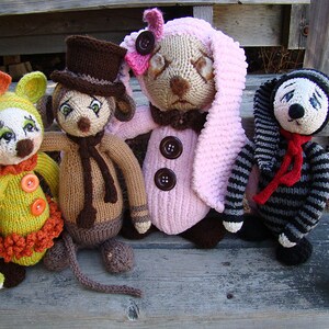 May include: Four knitted stuffed animals sitting on a wooden step. The animals are a green and orange clown, a brown and tan rabbit with a top hat, a pink bunny with a brown button nose, and a black and white striped dog with a red scarf.