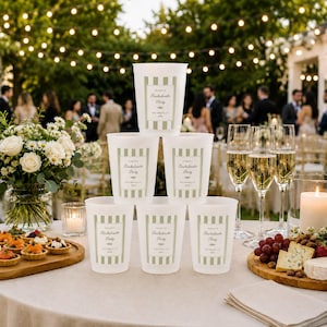 May include: A stack of six white plastic cups featuring a sage green vertical striped rectangular label with the text "Kailey's Bachelorette Party, San Diego, CA, 2024" printed in black, arranged in a pyramid formation on a table.