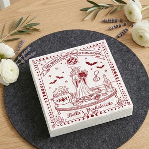 Pode incluir: Uma pilha de guardanapos de papel quadrados brancos com um design impresso em vermelho escuro de uma bruxa segurando flores, um caldeirão, uma bola de cristal e uma bola de discoteca. O texto diz This Witch is Getting Hitched e Bella's Bachelorette Est. 2025.