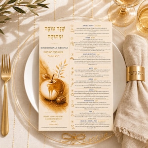 May include: A Rosh Hashanah blessings card with an apple and honey illustration, displayed on a white plate with a gold fork and napkin ring. The card includes Hebrew text and English translations, with a gold bow at the bottom.