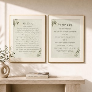 Op de afbeelding: Twee ingelijste wandkunstprints met het Shema-gebed in het Engels en Hebreeuws. Elke print heeft een lichtgroene achtergrond, donkergroene bladillustraties in de hoeken en zwarte tekst. De lijsten zijn dun en goudkleurig en tonen religieuze tekst.