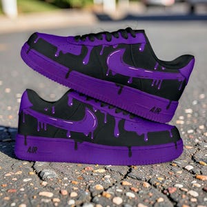 Op de afbeelding: Zwarte en paarse op maat gemaakte sneakers met een uniek druipontwerp. De schoenen hebben een zwarte basis met paarse accenten, waaronder het iconische swoosh-logo en een druipend verfeffect. Het woord "AIR" is zichtbaar op de tussenzool.
