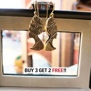 May include: A pair of gold-toned metal drop earrings featuring the profile of a figure wearing an ornate headdress. The earrings hang from curved wire hooks. Below the earrings, the text BUY 3 GET 2 FREE!! is printed in black and red.