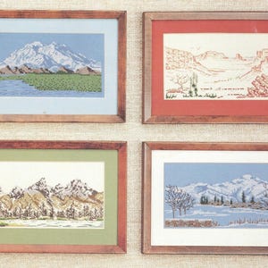 May include: Four rectangular framed cross-stitch landscapes. Top left: mountain with blue sky and green field. Top right: desert canyon with red matting. Bottom left: snowy peaks with green matting. Bottom right: winter scene with bare trees and white matting.