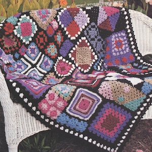 Puede incluir: Una manta de ganchillo hecha a mano con un patrón repetitivo de cuadrados de la abuela multicolores unidos con hilo negro. Los cuadrados incluyen varios tonos de rosa, morado, azul, rojo y beige, creando un textil vibrante y texturizado.