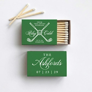 May include: Two green matchboxes with white text and a golf theme. One box says "Riley Caleb" with crossed golf clubs and "It's Us Forever." The other says "The Ashfords" with a date. Matches are visible.