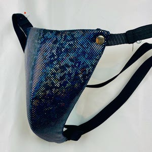 Pode incluir: Um suspensório azul e prateado com um tecido brilhante e texturizado. O suspensório tem alças elásticas pretas e um fecho de pressão dourado. Um alfinete vermelho está preso no topo.