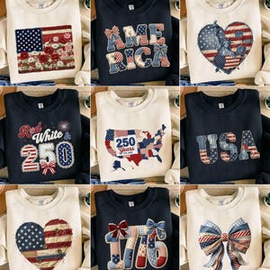 Könnte beinhalten: Eine Auswahl an cremefarbenen und marineblauen Sweatshirts mit patriotischen Designs. Die Designs umfassen die amerikanische Flagge, das Wort "AMERICA", ein Herz mit der Freiheitsstatue, eine Karte der USA, das Wort "USA", ein Herz mit der amerikanischen Flagge, die Zahl "1776" und eine Schleife.