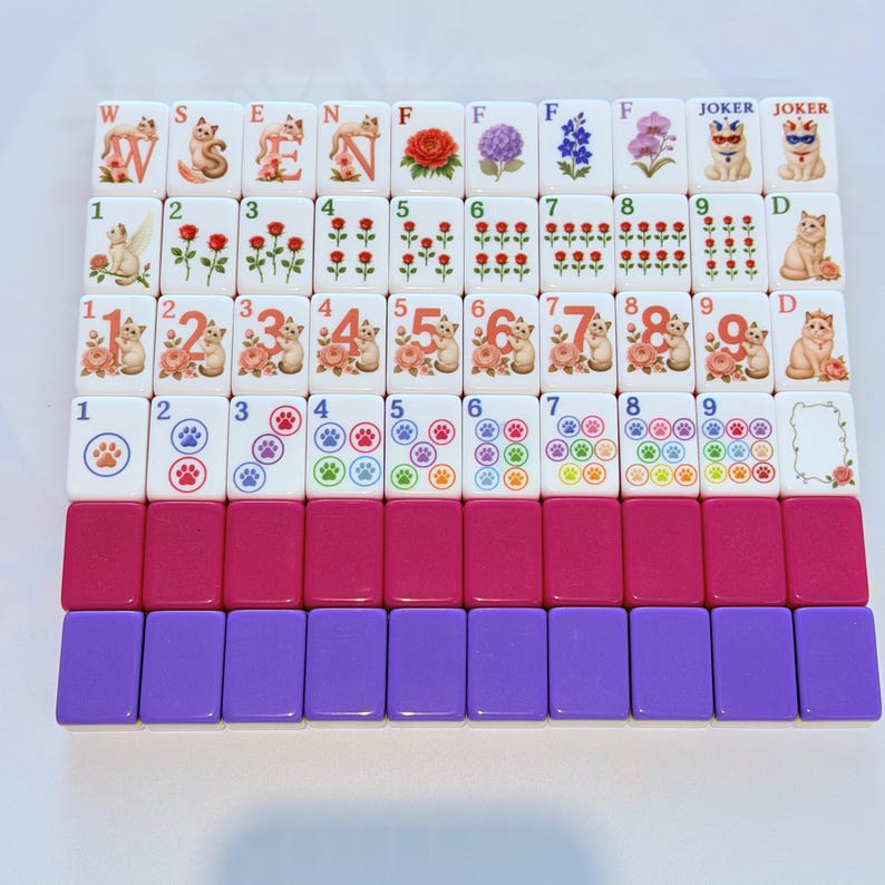 May include: A set of rectangular mahjong tiles featuring cat-themed illustrations, floral designs, numbers, and paw prints. The tiles are arranged in rows, with some displaying letters, joker labels, and blank spaces, alongside solid magenta and purple tiles.
