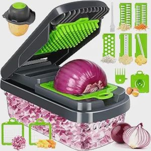 May include: A multi-functional vegetable chopper with a clear container filled with chopped vegetables. The chopper is black and green, with various interchangeable blades for different cuts. An uncut red onion sits in the chopper.