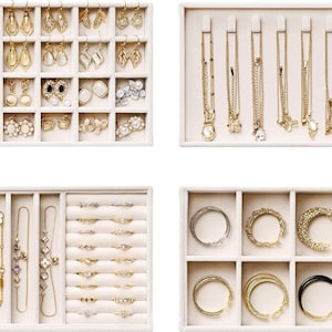 May include: A collection of gold-toned jewelry displayed in white trays. The trays contain earrings, necklaces, bracelets, and rings. The earrings vary in style, including studs and dangling designs. The necklaces feature pendants and delicate chains. The bracelets and rings are also in various styles.