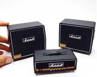 May include: Miniature black Marshall amplifiers with white trim and the Marshall logo. One amplifier has a handle and gold-colored knobs. The text "JCM 800 LEAD - 1960" is visible on the front of the amplifiers.