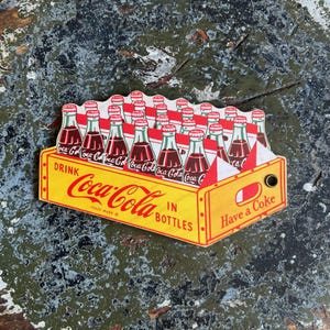 Folleto con figuras de la planta embotelladora de Coca-Cola de los años 50 • Caja troquelada con forma de botella • Folleto ilustrado de visita a la fábrica