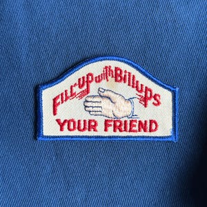 May include: A blue fabric with a rectangular patch featuring the text "Fill up with Billups YOUR FRIEND" in red and a hand illustration. The patch has a white background with a blue border.