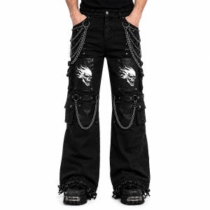 Puede incluir: Pantalones negros de pierna ancha con múltiples bolsillos cargo, cadenas metálicas plateadas unidas a anillas en D y estampados gráficos blancos de calaveras en llamas en los muslos. Incluye correas laterales ajustables y herrajes metálicos.