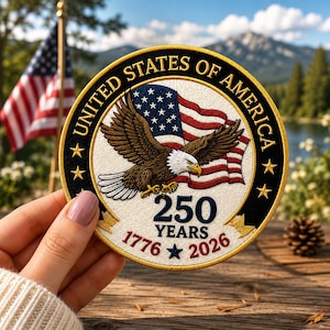 May include: Embroidered patch featuring an American flag and a bald eagle with outstretched wings. The patch is circular, with the text "UNITED STATES OF AMERICA" and "250 YEARS 1776-2026". The patch has a black border with gold stars.