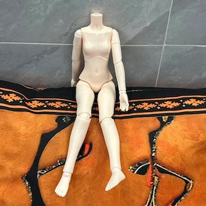 Può includere: Un corpo di bambola articolato a snodi sferici di colore pallido con una finitura liscia e opaca. La figura presenta un busto definito, articolazioni mobili su spalle, gomiti, polsi, anche, ginocchia e caviglie, con mani e piedi dettagliati.