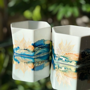 May include: Two white hexagonal ceramic planters with gold leaf designs and blue and orange watercolor accents.