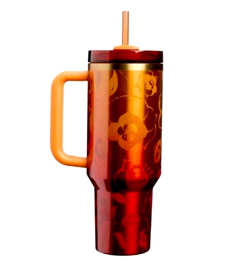 May include: A tall, cylindrical tumbler with a metallic red finish and a repeating orange floral pattern. It features a sturdy orange side handle, a gold-toned rim, a dark red lid, and a matching orange straw extending from the center of the top.