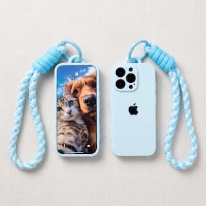 May include: A light blue smartphone case with a matching braided rope wrist strap. The case features a cutout for the camera lens and an Apple logo on the back. The phone screen displays a photograph of a tabby cat and a golden dog.