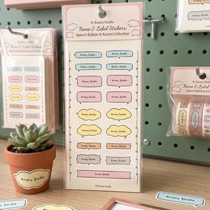 Può includere: Un foglio verticale di adesivi Name & Label Stickers: Speech Bubble & Accent Collection di Aruary Studio. Il foglio contiene due colonne di adesivi a forma di fumetto color pastello in blu, rosa, giallo, marrone e grigio, con testo.