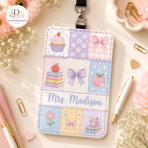 May include: A rectangular ID badge holder with a black lanyard clip, featuring a patchwork design of pastel-colored squares with illustrations of cupcakes, apples, books, bows, and flowers. The text Mrs. Madison is printed in blue script.