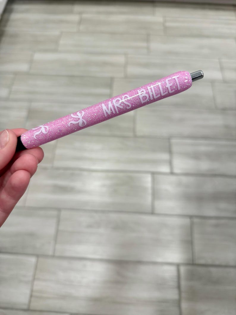 Puede incluir: Un bol&iacute;grafo rosa brillante con el texto "MRS. BILLET" en blanco. El bol&iacute;grafo tiene una punta plateada y una base negra. El bol&iacute;grafo se sostiene en una mano.
