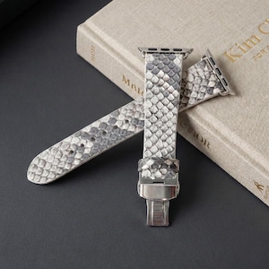 May include: A watch band featuring a gray and white snakeskin pattern with a textured scale finish. The band includes silver-toned metal attachment hardware at the top and a polished silver-toned metal deployment clasp at the bottom end.