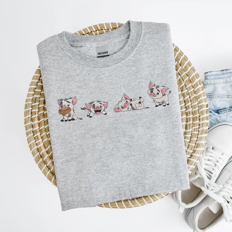 May include: A light grey crew neck sweatshirt with an embroidered design of four cartoon pigs in various poses. The pigs are pink, black, and white. The sweatshirt is made of a soft material.
