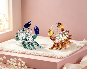 May include: Two glass crab figurines, one in shades of blue and green and the other in amber and brown, both featuring white polka dot patterns on their shells and raised claws. These translucent sculptures are crafted with smooth, glossy surfaces.