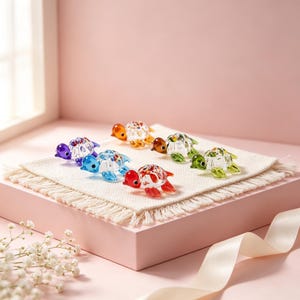 Puede incluir: Una colección de cinco pequeñas figuras de tortugas de cristal en varios colores, incluyendo morado, azul, naranja, rojo y verde. Cada tortuga presenta un caparazón de cristal transparente con detalles coloridos y aletas.