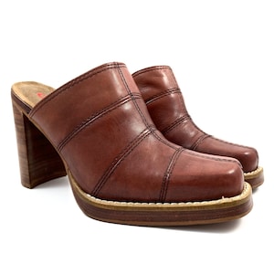 Op de afbeelding: Bruine leren klompen met hak, vierkante neus en een dikke houten hak.