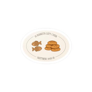 May include: An oval sticker with a cream background featuring a brown line drawing of two fish and a stack of five loaves of bread. The text reads 12 BASKETS LEFT OVER at the top and MATTHEW 14:13-21 at the bottom in a dark brown serif font.