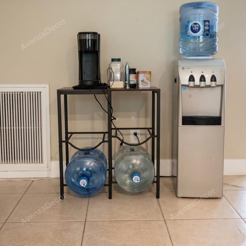 May include: A black metal stand holds a black coffee maker and various containers on top, with two large clear plastic water jugs stored on the bottom shelf. Beside the stand is a silver water cooler with a large blue-labeled water jug on top.