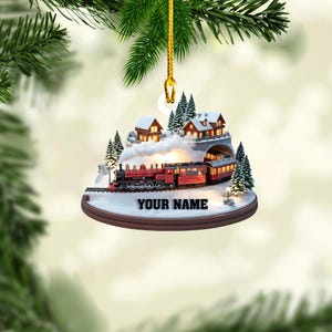 May include: A circular Christmas ornament featuring a 3D winter scene with a red steam train traveling through a snowy landscape. The scene includes illuminated houses, evergreen trees, and a tunnel. The text YOUR NAME is printed on the base.