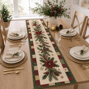 May include: A rectangular quilted table runner featuring a central garland of red poinsettias, green holly leaves, pine cones, and small gold stars on a cream background, bordered by a patchwork pattern of red, green, and tan squares.