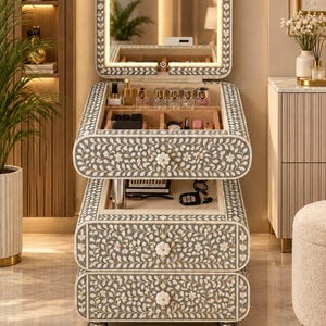 May include: A grey and white floral inlay vanity table featuring a flip-top mirror with integrated LED lighting, two lower drawers, and an upper storage compartment containing various cosmetic bottles and containers with flower-shaped knobs.