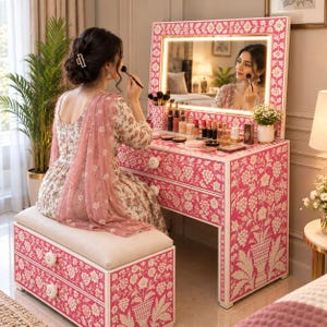 Può includere: Un tavolo da trucco con panca abbinata caratterizzato da un motivo floreale intarsiato rosa e bianco. Il tavolo include uno specchio rettangolare con illuminazione a LED integrata, due cassetti con pomelli floreali bianchi e vari trucchi.