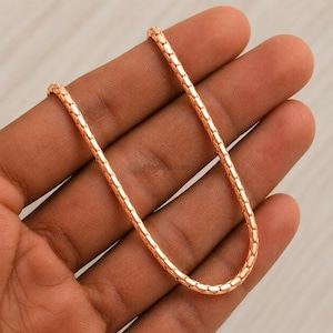 May include: A rose gold-toned chain necklace featuring a rounded, textured link design. The chain has a polished, metallic finish with a repeating pattern of small, interconnected oval segments that create a smooth, continuous, and flexible structure.