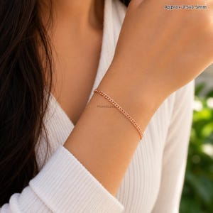 Op de afbeelding: Een delicate roségouden kettingarmband met kleine, in elkaar grijpende gourmet schakels. Het armbandje is gemarkeerd met afmetingen van ongeveer 3,5 x 1,5 cm. Het metaal heeft een gepolijste, reflecterende afwerking die het licht opvangt.