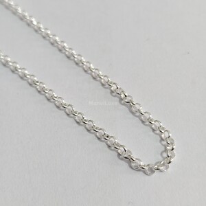 May include: A silver-colored rolo chain necklace featuring a series of uniform, round, interlocking links. The metal surface has a reflective, polished finish. The text ManviLuxe is printed in small, light-colored letters near the center of the chain.