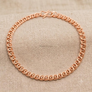 Op de afbeelding: Een roségouden kettingarmband met een reeks in elkaar grijpende ronde schakels. De armband is opgebouwd uit een consistent patroon van afgeronde metalen lussen en wordt vastgezet met een eenvoudige S-vormige haaksluiting aan de bovenzijde.
