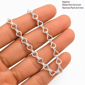 Op de afbeelding: Een zilverkleurige metalen ketting met herhalende druppelvormige schakels. De tekst op de afbeelding geeft afmetingen aan van ongeveer 5x1mm voor het brede deel en 2x1mm voor het smalle deel van de schakels van dit metalen sieraadonderdeel.