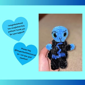 May include: A handmade blue and black crochet doll with green eyes. The doll has blue arms and head, and a black body with blue accents. The image also includes two blue heart-shaped graphics with text.