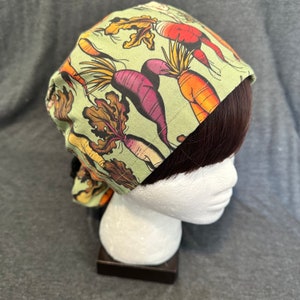 Peut inclure: Un bonnet de chirurgien vert avec un imprimé coloré de carottes et de radis. Le bonnet a une cravate à l'arrière.